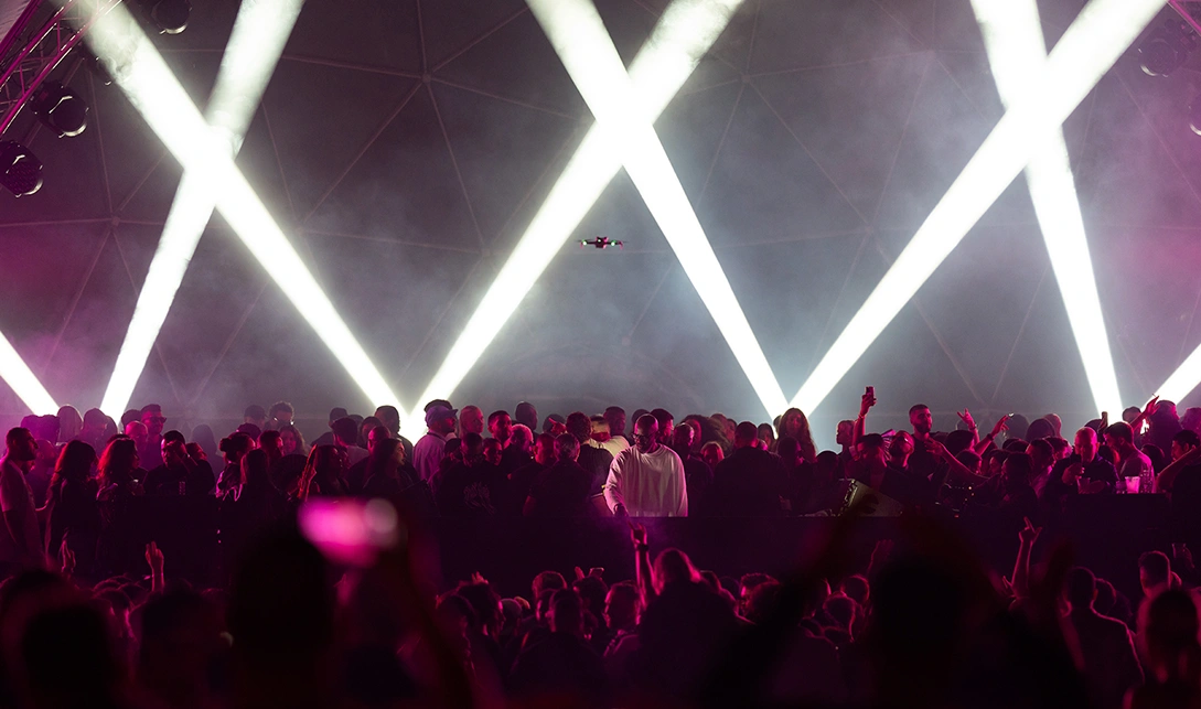 Concert crowd with bright lights and drone in the air.